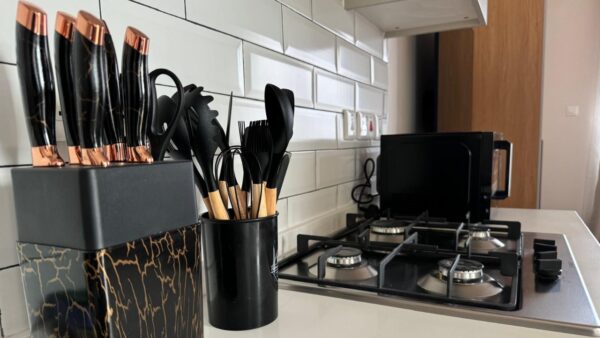 Knife set and utensils on a counter beside a gas stove with two burners, against a white subway tile backsplash.