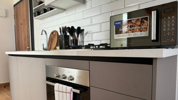 Modern kitchen with a stove, mounted oven, microwave, white subway tile backsplash, and utensils organized on the counter.