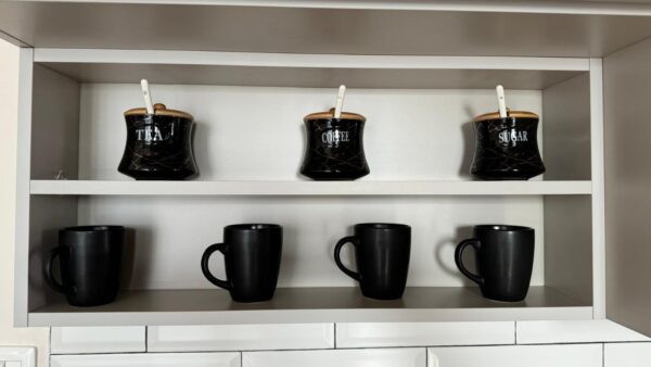 Black shelves with tea, coffee, and sugar jars on top; four black mugs on the bottom.