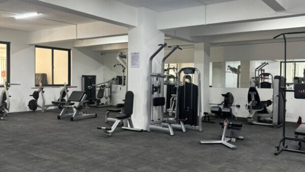 Spacious gym with weight machines, benches, and mirrors on white walls.