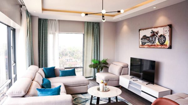 Modern living room with L-shaped sofa, blue cushions, potted plant, TV, and motorcycle painting on the wall.