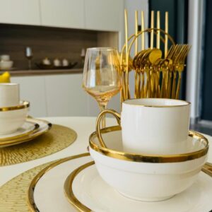 Elegant dinnerware with gold trim, including plates, cup, glasses, and gold utensils on a white table.
