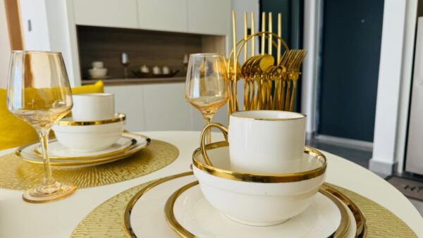 Elegant dinnerware with gold trim, including plates, cup, glasses, and gold utensils on a white table.
