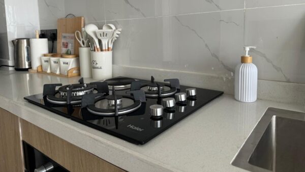 Modern kitchen with a black stove, white utensil holder, tea and coffee canisters, and a liquid soap dispenser by the sink.