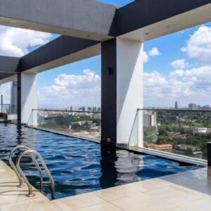 Rooftop infinity pool with city skyline view, surrounded by modern architecture, lounge chairs, and clear blue sky.