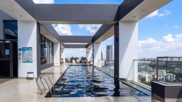 Rooftop pool with modern glass railings and city skyline view under a partly cloudy sky.