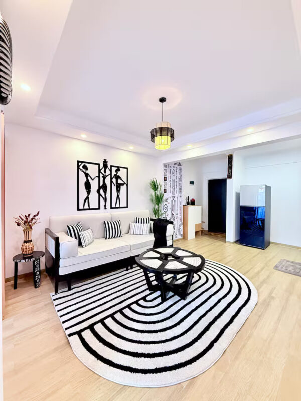 Modern living room with white sofa, striped pillows, black-and-white geometric rug, framed art, and pendant light.