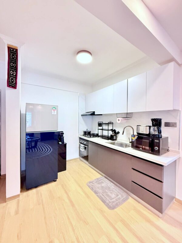Modern kitchen with white cabinets, stainless steel appliances, black refrigerator, and wooden floor; countertop with sink and coffee maker.