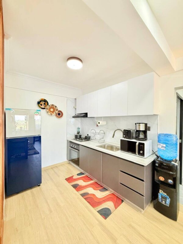 Modern kitchen with dark cabinets, white countertop, stainless steel sink, appliances, blue fridge, decorative plates, and a wood floor.