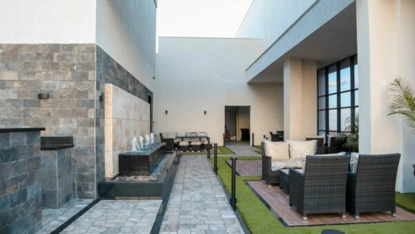 Modern patio with wicker furniture, a narrow water fountain on stone paving, and large windows.