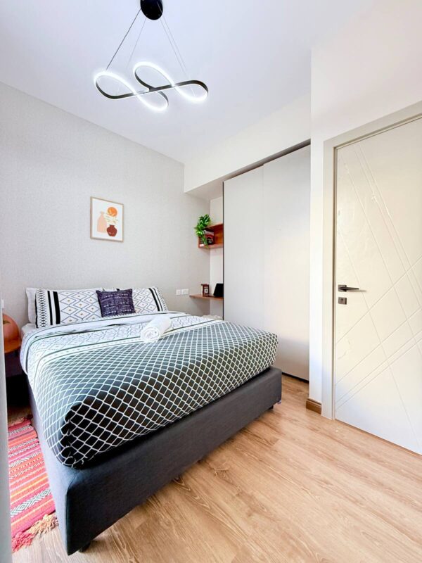 Modern bedroom with geometric-patterned bedding, art, plant, sleek light fixture, and wooden floor.