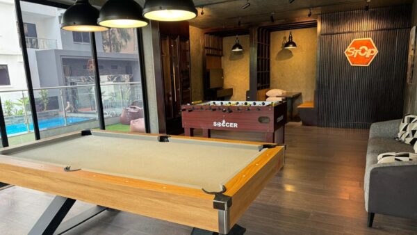 Game room with a pool table, foosball, couch, glass wall, outside view of pool, and bean bags with modern lighting.