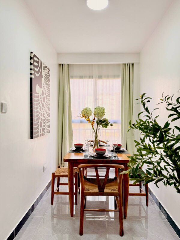Cozy dining area with a wooden table set for four, featuring a floral centerpiece, near a window with light curtains.