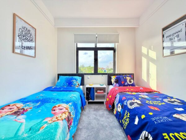 Two twin beds with colorful themed bedding, artwork on the walls, and a window between them letting in natural light.