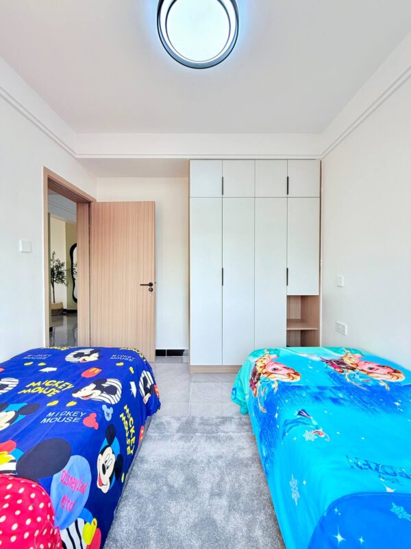 Bedroom with two single beds, Mickey Mouse and Frozen-themed blankets, wooden wardrobe, and circular ceiling light.
