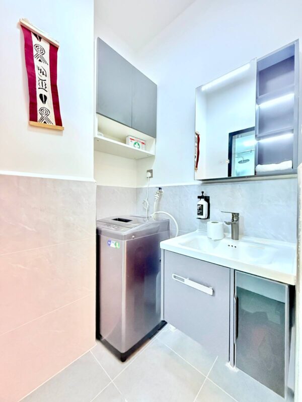 Laundry room with a washing machine, sink, and cabinets. Wall art and shelves with a first aid kit visible.