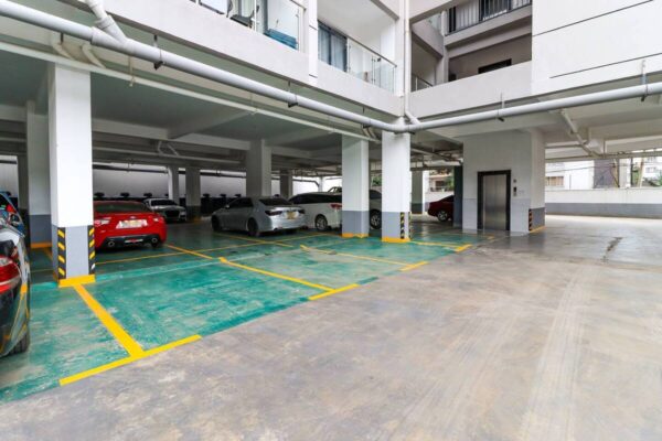 Covered parking area with multiple cars, empty spaces, and an elevator in a residential building.
