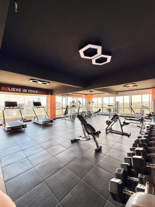 Modern gym with treadmills, weight machines, dumbbells, motivational quotes on walls, and large windows with city views.