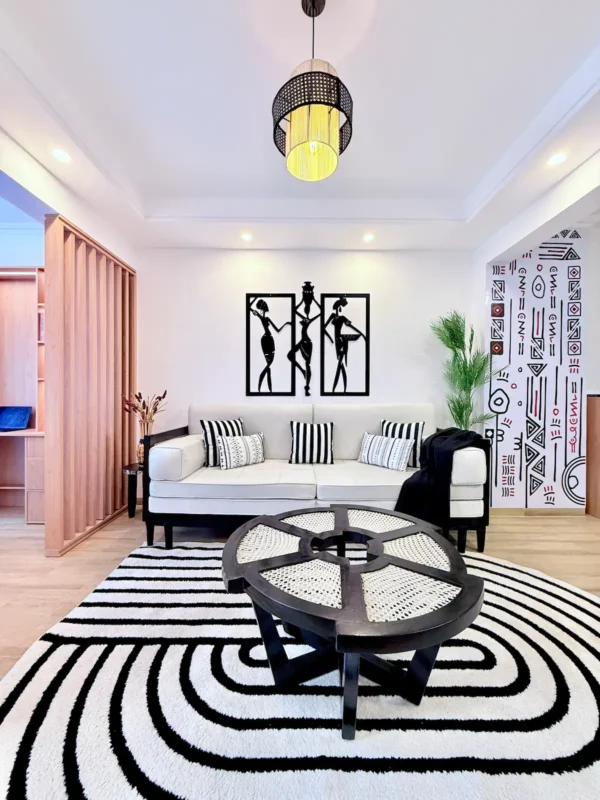 Modern living room with a white sofa, black and white decor, abstract art, and a round coffee table on a striped rug.