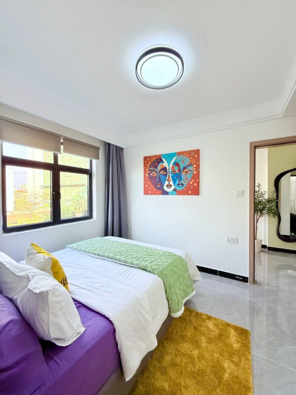 Modern bedroom with a double bed, colorful bedding, abstract wall art, and natural light from a large window.