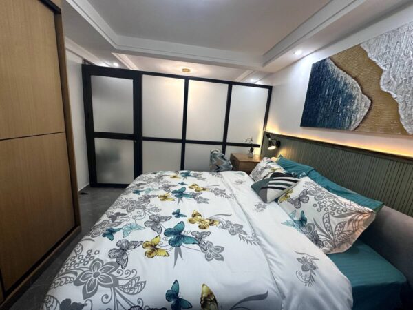 Cozy bedroom with butterfly-patterned bedding, abstract wall art, and soft lighting behind a modern frosted glass partition.