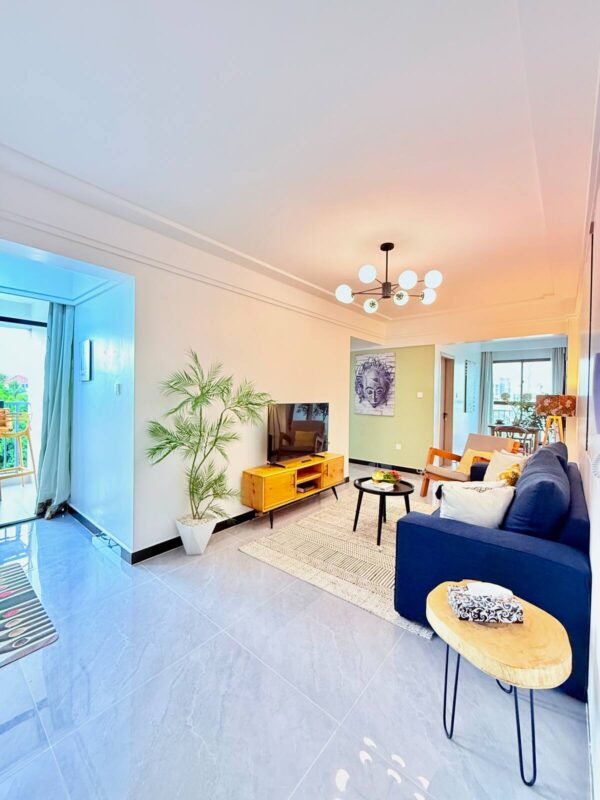 Modern living room with a navy sofa, wooden TV stand, round coffee table, potted plant, and a geometric chandelier.