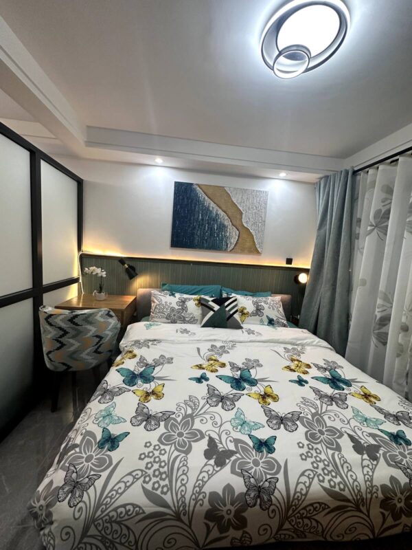 Cozy bedroom with butterfly-patterned bedding, abstract wall art, modern chair, and soft lighting under a circular ceiling light.
