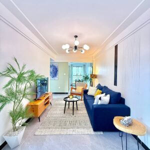 Modern living room with a navy sofa, decorative pillows, wooden furniture, potted plants, and a geometric rug under a stylish lamp.