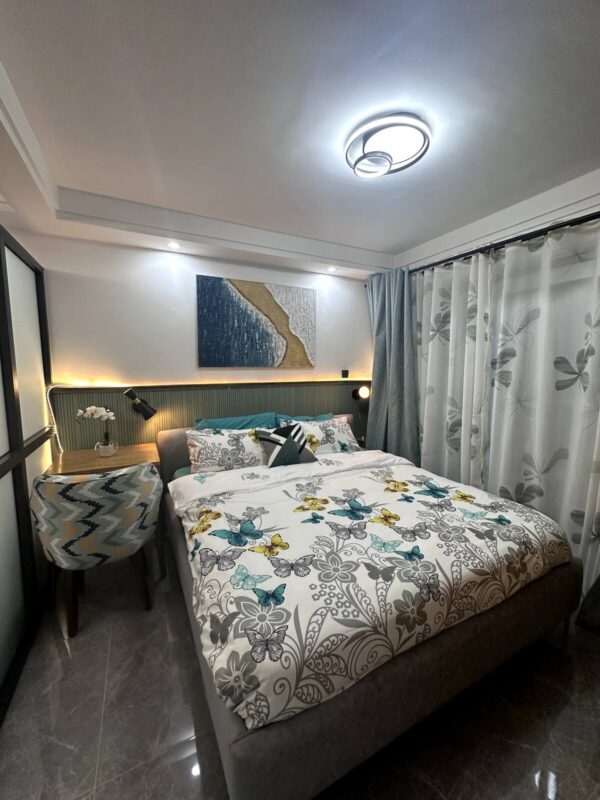 Cozy bedroom with butterfly-themed bedding, abstract wall art, modern ceiling light, and a patterned chair by a wooden table.