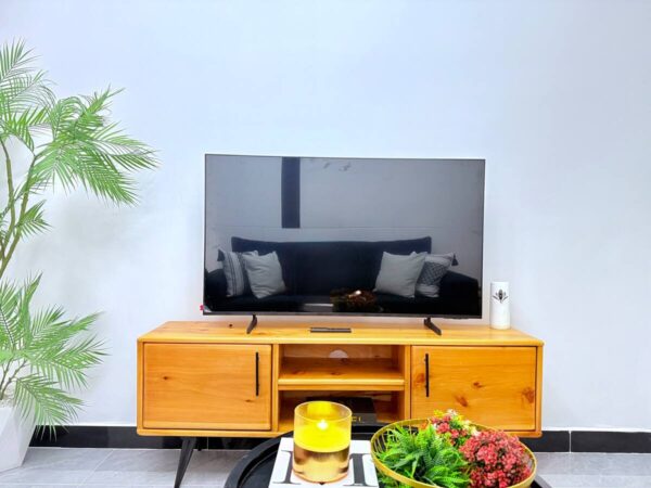 TV on a wooden stand with a potted plant to the left and a yellow candle and flowers in the foreground.