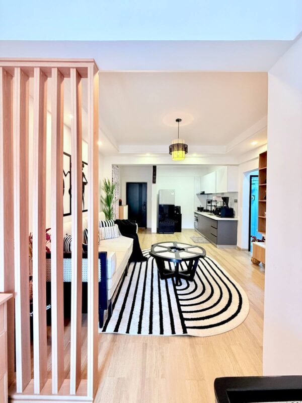 Modern living room with a beige sofa, black-and-white striped rug, round coffee table, and open kitchen in the background.