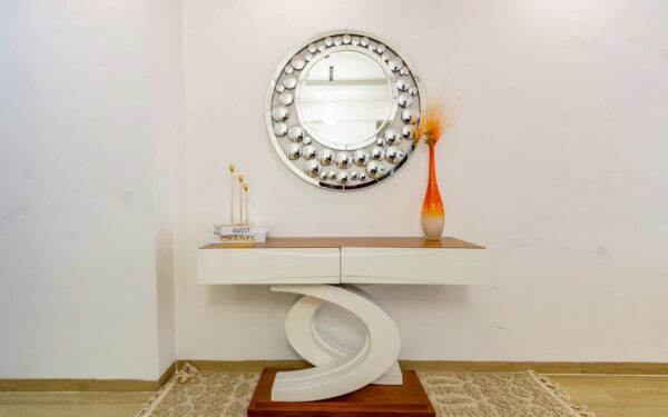 Modern console table with curved base, circular mirror, orange vase, and decorative books on top.