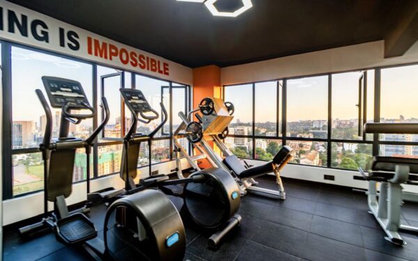 Gym with exercise machines, large windows showing cityscape, motivational text on wall, well-lit interior.
