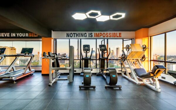 Bright gym with city view, treadmills, stationary bikes, leg press machine, and motivational text: "Nothing is Impossible."