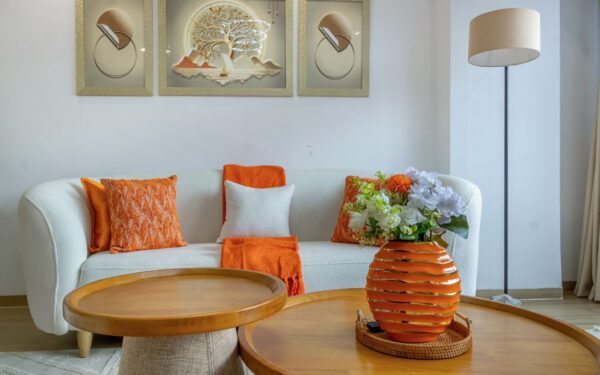 Cozy living room with white sofa, orange accents, floral arrangement in striped orange vase, and modern wall art.